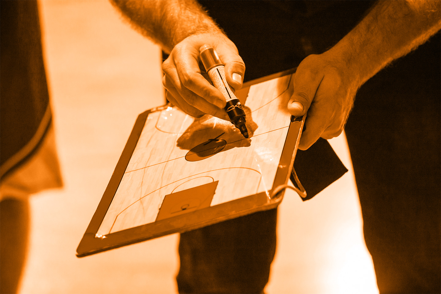 Erudite coach writing on a basketball court clipboard